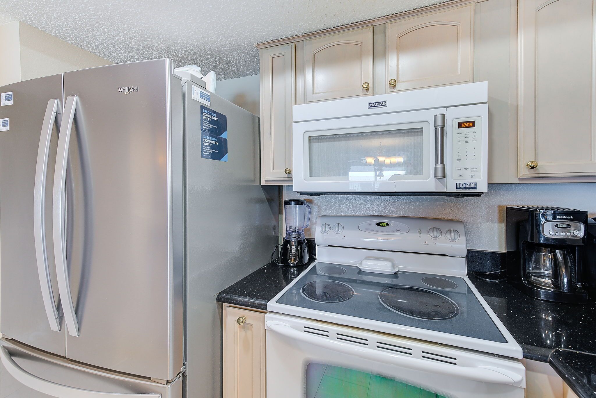 A compact kitchen with a stainless steel refrigerator, a microwave, an electric stove, and a coffee maker.
