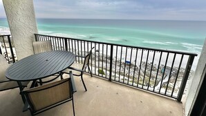 Ein Balkon mit Tisch und Stühlen, der auf einen Strand mit Blick auf das Meer und eine ferne Küste blickt.