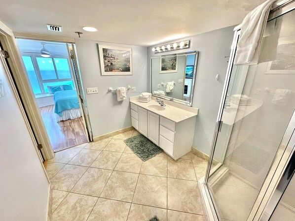 A bathroom with a large mirror, a sink, and a shower. There is a rug on the floor and a painting on the wall. - Fabulous views! Beachfront Unit! 4135 BS1 (Miramar Beach)