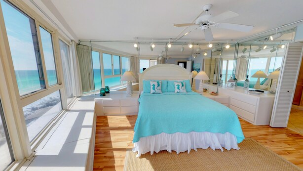 Ein geräumiges Schlafzimmer mit einem großen Bett, einem Deckenventilator und Meerblick durch große Fenster.