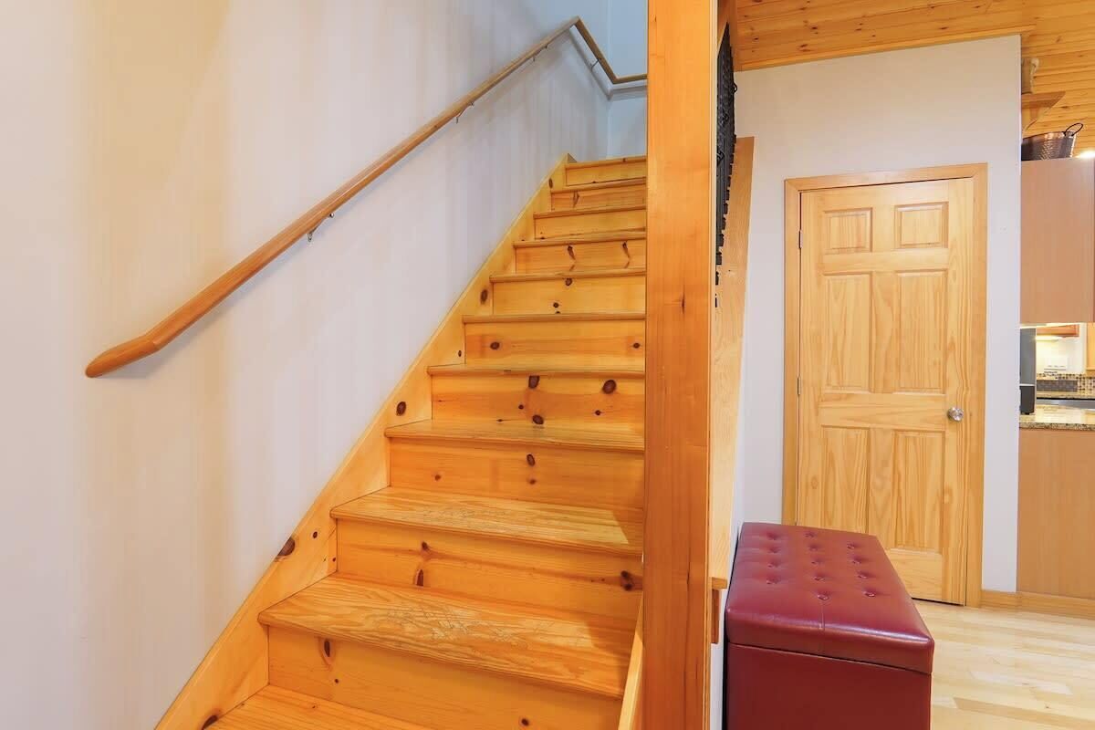 A wooden staircase leading to a room with a wooden door and a red bench.