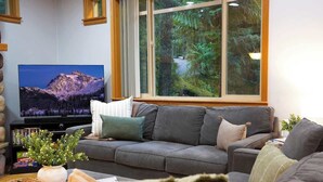 Ein Wohnzimmer mit großem Fenster, einer Couch, einem Fernseher und einem Bücherregal.