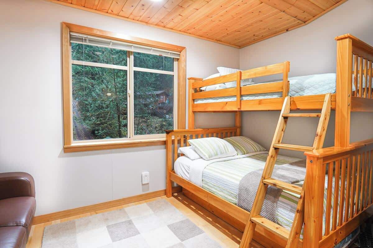 A bunk bed room with a window, a brown leather chair, and a checkered rug.