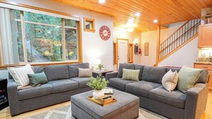 Ein Wohnzimmer mit zwei grauen Sofas, einem Couchtisch mit einer Pflanze, einer Uhr und einer Treppe, die zur Küche führt.