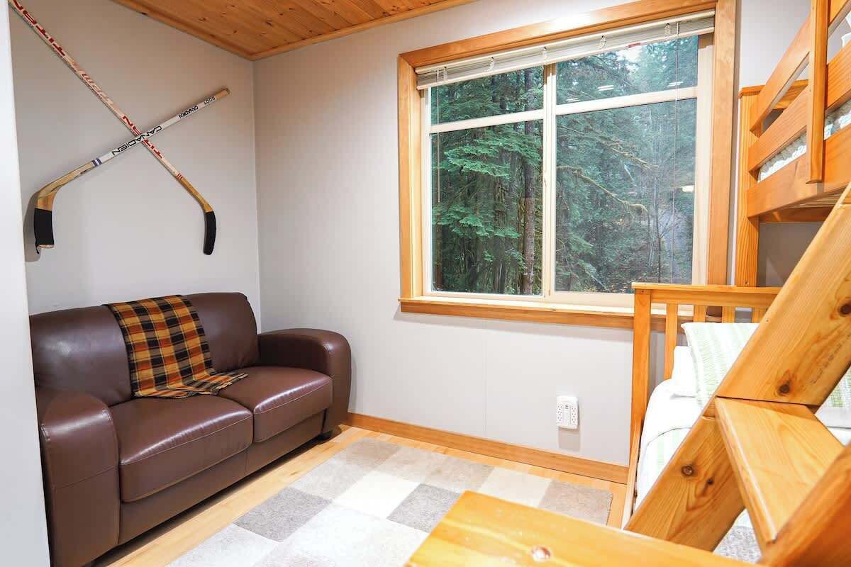Una habitación acogedora con un sofá de cuero marrón, una manta de cuadros, un banco de madera y una ventana con vistas a árboles.
