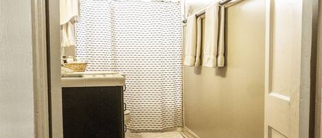 Un baño estrecho con cortina de ducha a rayas, un lavamanos pequeño y un perchero para toallas.