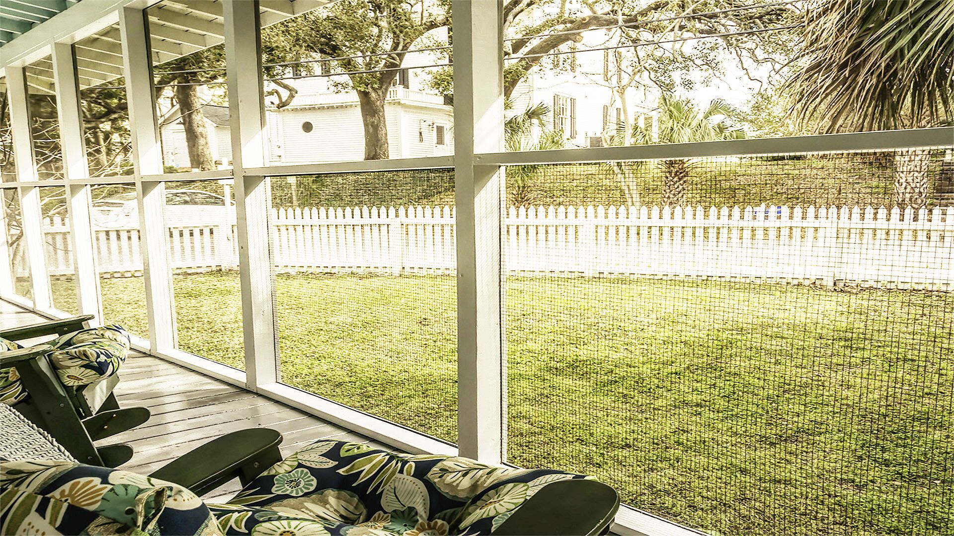 A covered porch with a view of a white picket fence and a grassy yard.