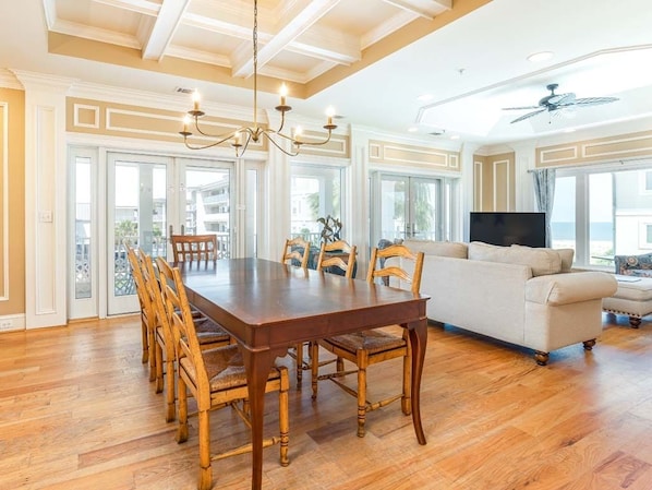 A spacious living room with a wooden dining table and chairs, a beige sofa, and a television.