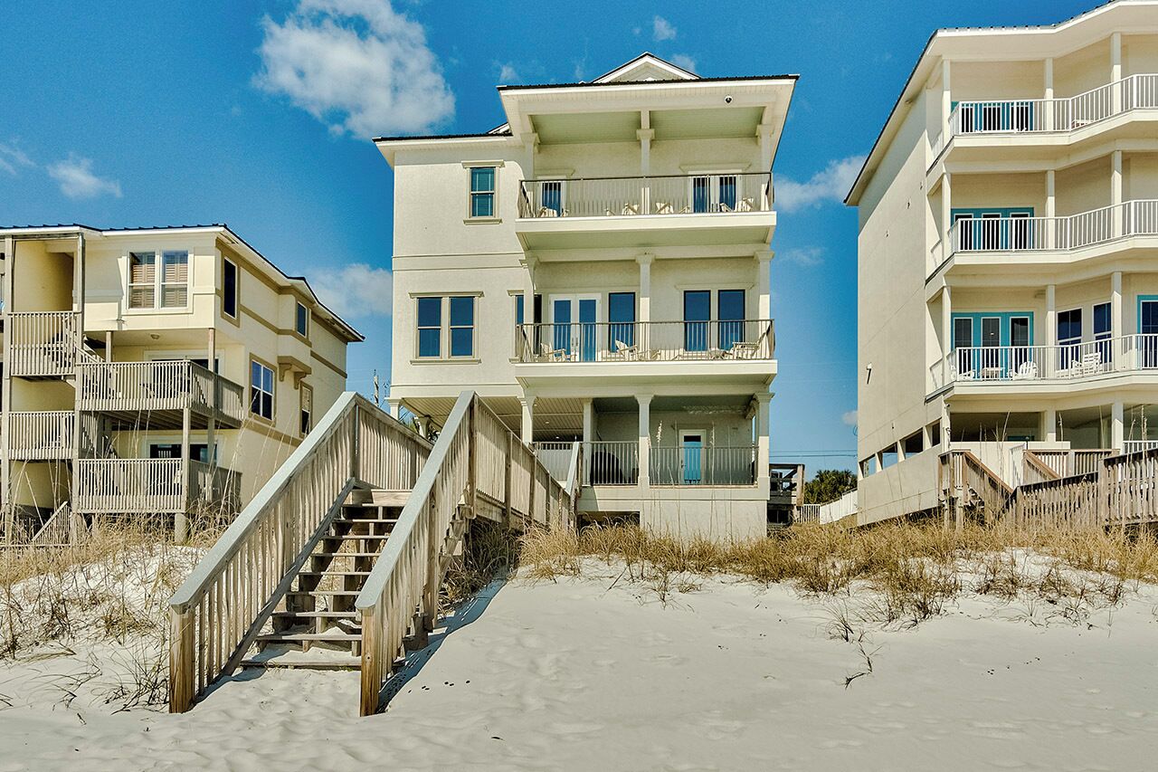A beachfront hotel with multiple balconies, a central entrance, and a wooden staircase leading to the beach.