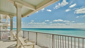 A balcony with white chairs overlooking a beach.