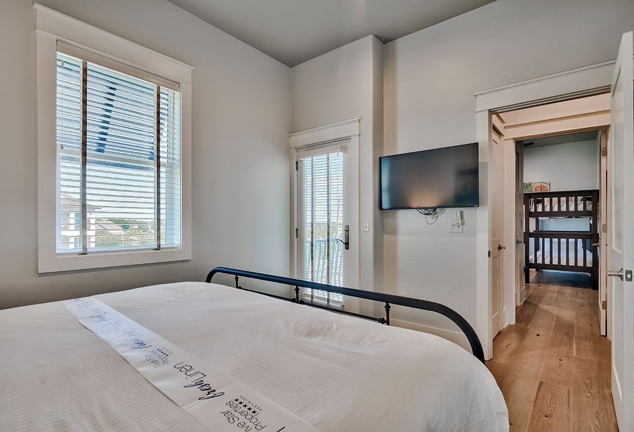 Ein Schlafzimmer mit einem Bett, einem an der Wand montierten Fernseher und einer Tür, die auf einen Balkon führt.