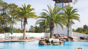 Zona de piscina con sillones de descanso, palmeras y una formación rocosa.