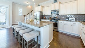 Una cocina moderna con armarios blancos, encimera de granito y una isla central con taburetes de bar.