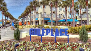 Señal de Gulf Place con una fila de palmeras y un edificio con balcones al fondo.