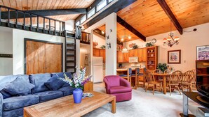 A spacious living area with a sofa, a coffee table, and a dining table set for four. A staircase leads to an upper level. - Enchanting Mountain Haven: Ski, Explore & Relax with Unrivaled VIEWS! (Breckenridge)
