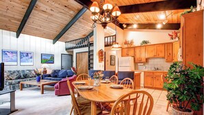 A cozy living room with a wooden ceiling, a dining table set for four, and a kitchen with wooden cabinets. - Enchanting Mountain Haven: Ski, Explore & Relax with Unrivaled VIEWS! (Breckenridge)