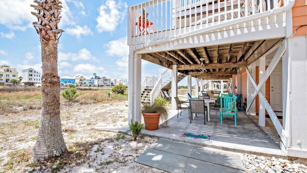 A covered outdoor area with a wooden deck, a small table, chairs, and a potted plant. - ShellChase | 5BR/3.5BA Martinique Home | Sleeps 12 | Gulf Views + Pool (GULF SHORES)