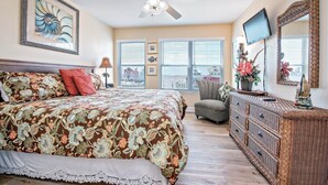 A bedroom with a large bed, a ceiling fan, a dresser, a chair, and a TV on the wall. - ShellChase | 5BR/3.5BA Martinique Home | Sleeps 12 | Gulf Views + Pool (GULF SHORES)