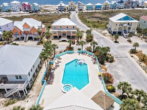 A resort with a central swimming pool, multiple buildings, and a beach view.