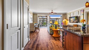 A hotel lobby with a wooden floor, wicker furniture, a central seating area, and a view of the building's exterior.