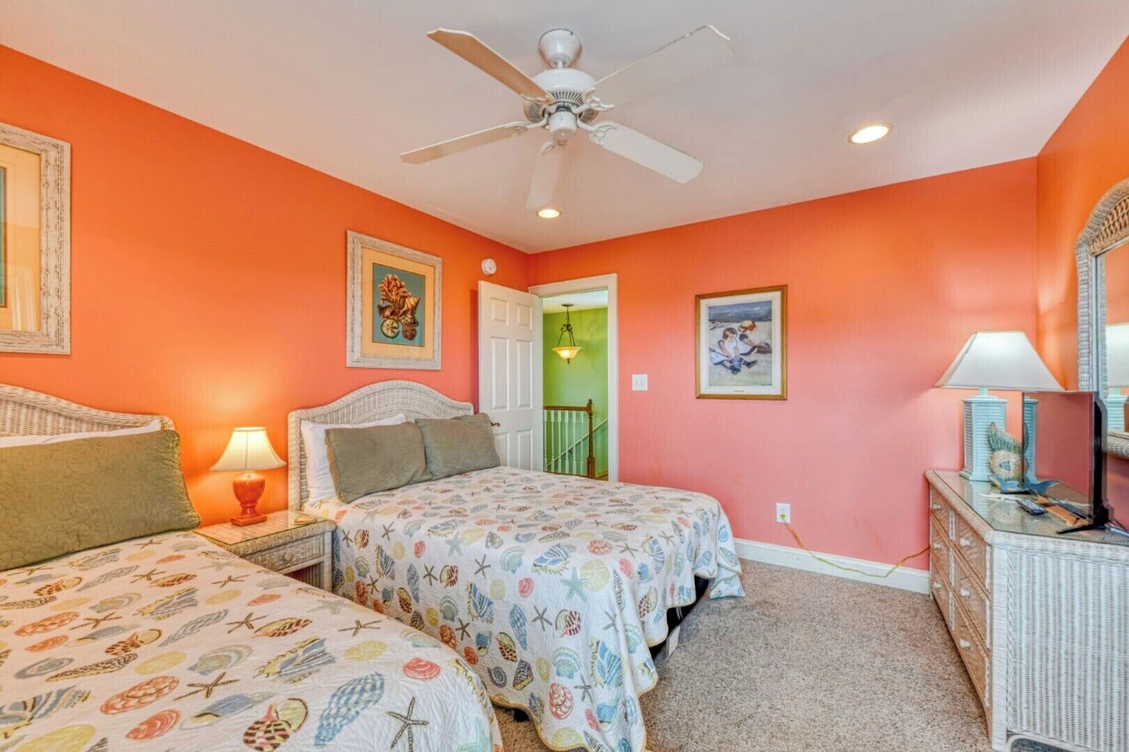 Une chambre avec deux lits, un ventilateur de plafond et une commode avec un miroir.