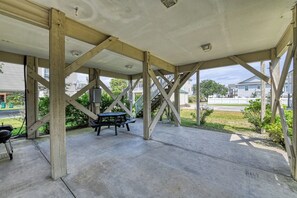 A covered patio area with a picnic table and grill, supported by wooden beams.