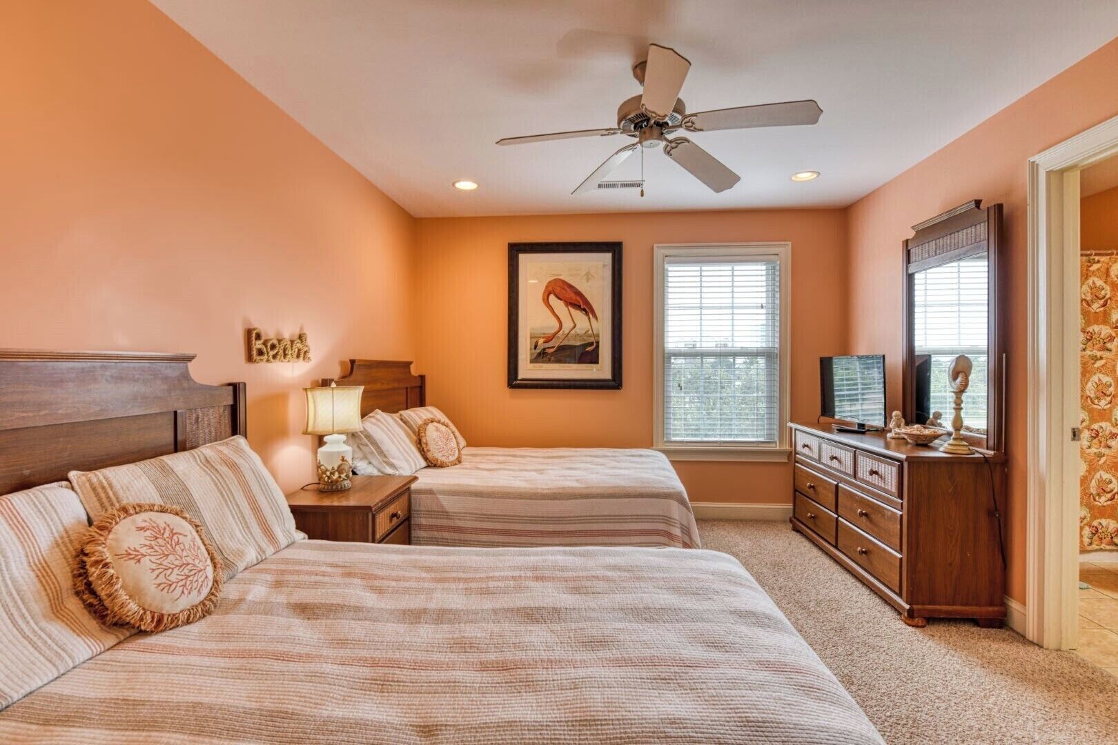 A bedroom with two beds, a ceiling fan, a dresser, a television, and a window with blinds.