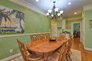 A dining area with a wooden table and chairs, a chandelier, and a painting of a sailboat on the wall.