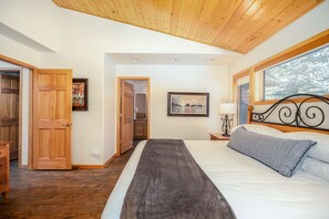 A bedroom with a wooden ceiling, a bed with a gray blanket, a nightstand with a lamp, and a framed picture on the wall.