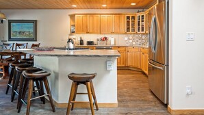 Una cocina moderna con armarios de madera, un refrigerador de acero inoxidable y una barra con taburetes.