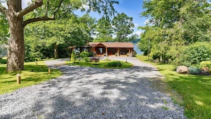 A lodge with a gravel driveway leading to a wooden deck and a lake view.