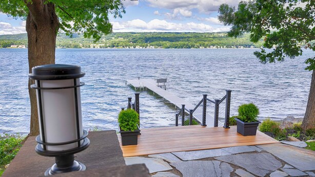 A lakeside deck with a lamp, potted plants, and a view of the lake and distant hills.
