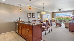 A modern kitchen with a central island, dining area with chairs, and a living room with a view.