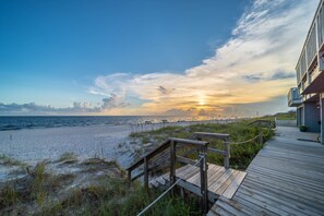 Pasarela de madera que conduce a una playa con un atardecer de fondo.