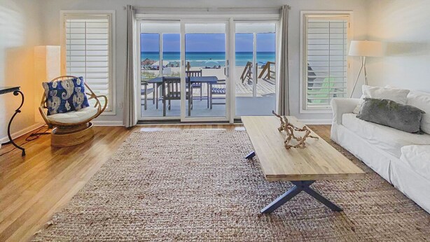 A spacious living room with a large sliding glass door leading to a balcony with a view of the beach.