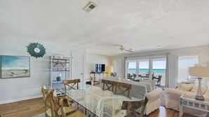 A spacious living area with a glass dining table, wooden chairs, a white sofa, and a view of the ocean through large windows.