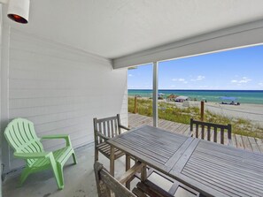Un balcón con vista a la playa, una silla verde y una mesa de madera.