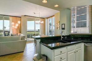 A modern kitchen with a large island, white cabinetry, and a view to the outside.