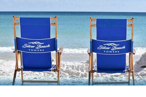 Two beach chairs with "Silver Beach Towers" branding on a sandy beach with ocean waves in the background.