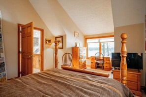 A bedroom with a large bed, wooden dresser, desk, and chair, a television, and a window with a view.