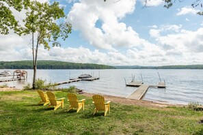 Relax by the serene lake with a grassy area, Adirondack chairs, and a wooden dock.