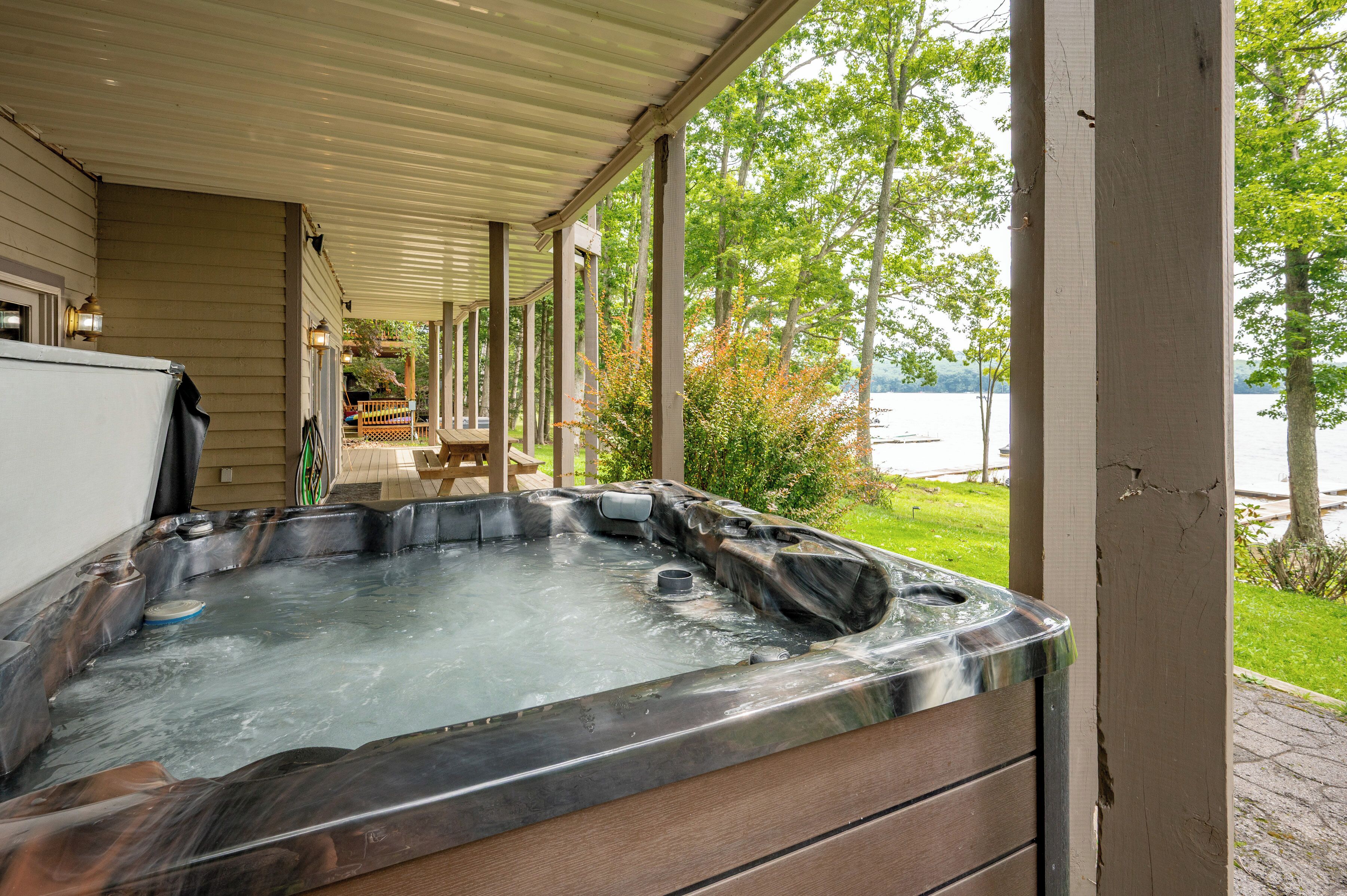 A hot tub under a covered porch with a view of a lake and trees.