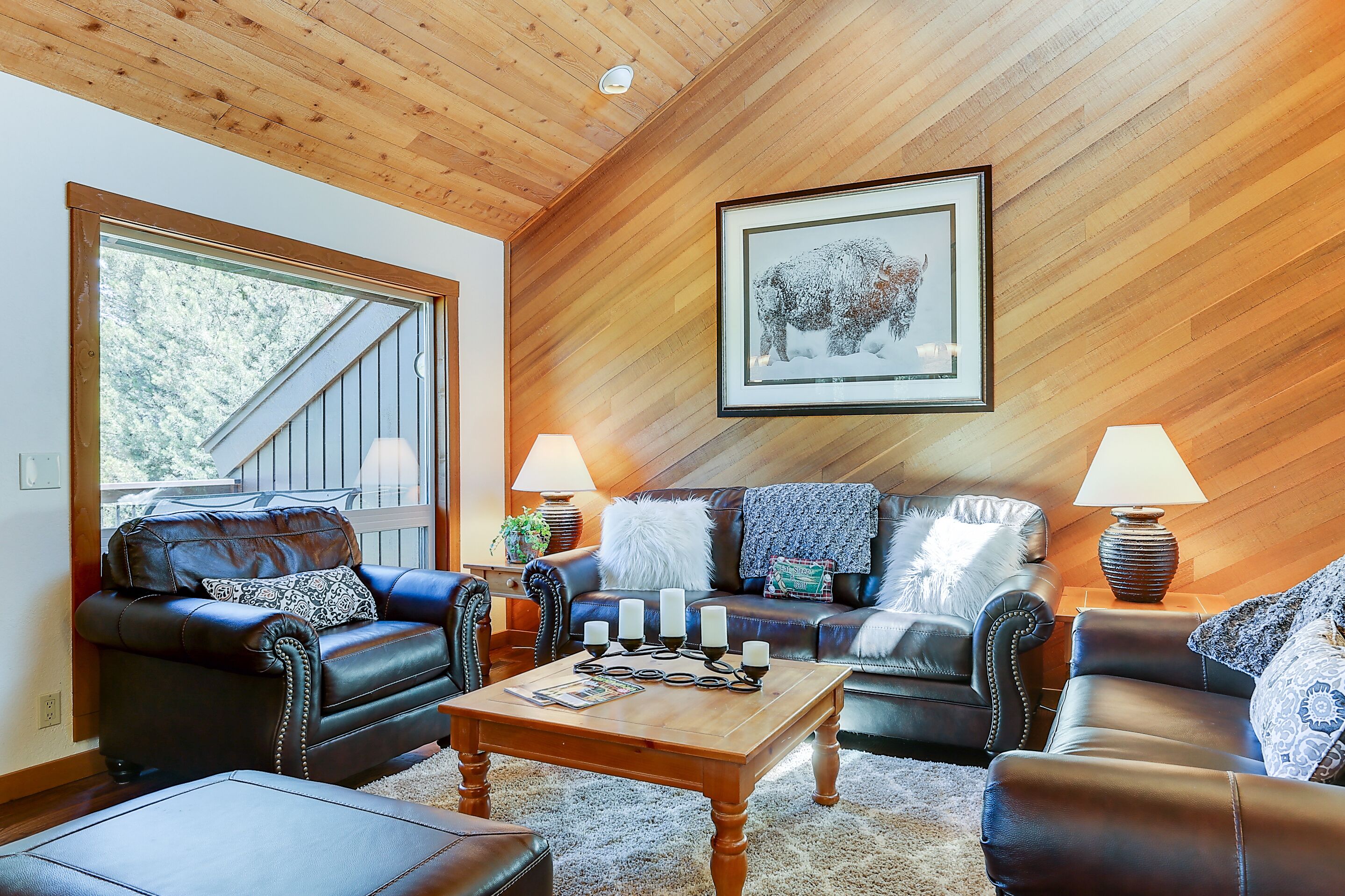 A cozy living room with a wooden ceiling, leather sofas, a coffee table, and a framed picture on the wall.