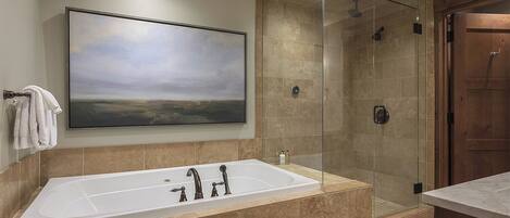 A modern bathroom with a large bathtub, a glass-enclosed shower, and a wooden door.