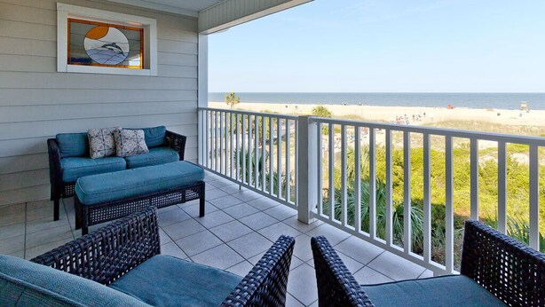 Ein Balkon mit Rattanmöbeln, einem gerahmten Kunstwerk und Blick auf den Strand.