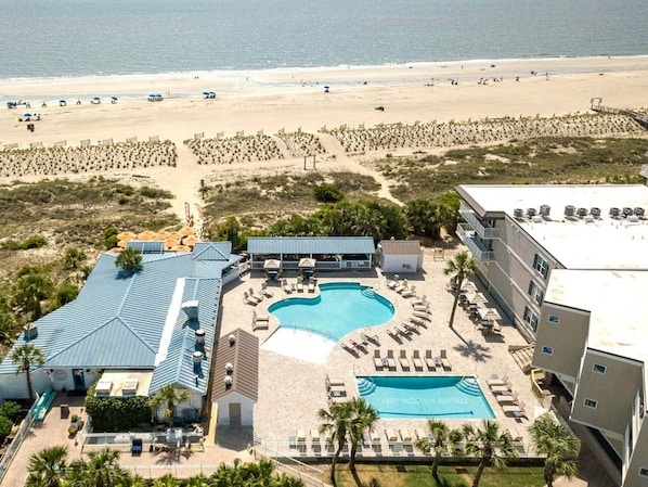 An aerial view of a resort with a swimming pool, beach access, and a beachside promenade.