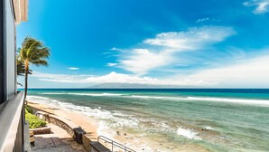 Vista al mar desde un balcón con una palmera, cielo despejado y olas.