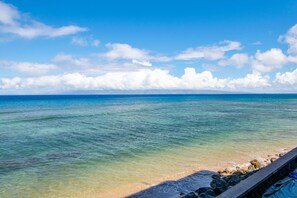 En strand med krystalklart turkisblåt vand, en stenet kystlinje og en klar himmel.