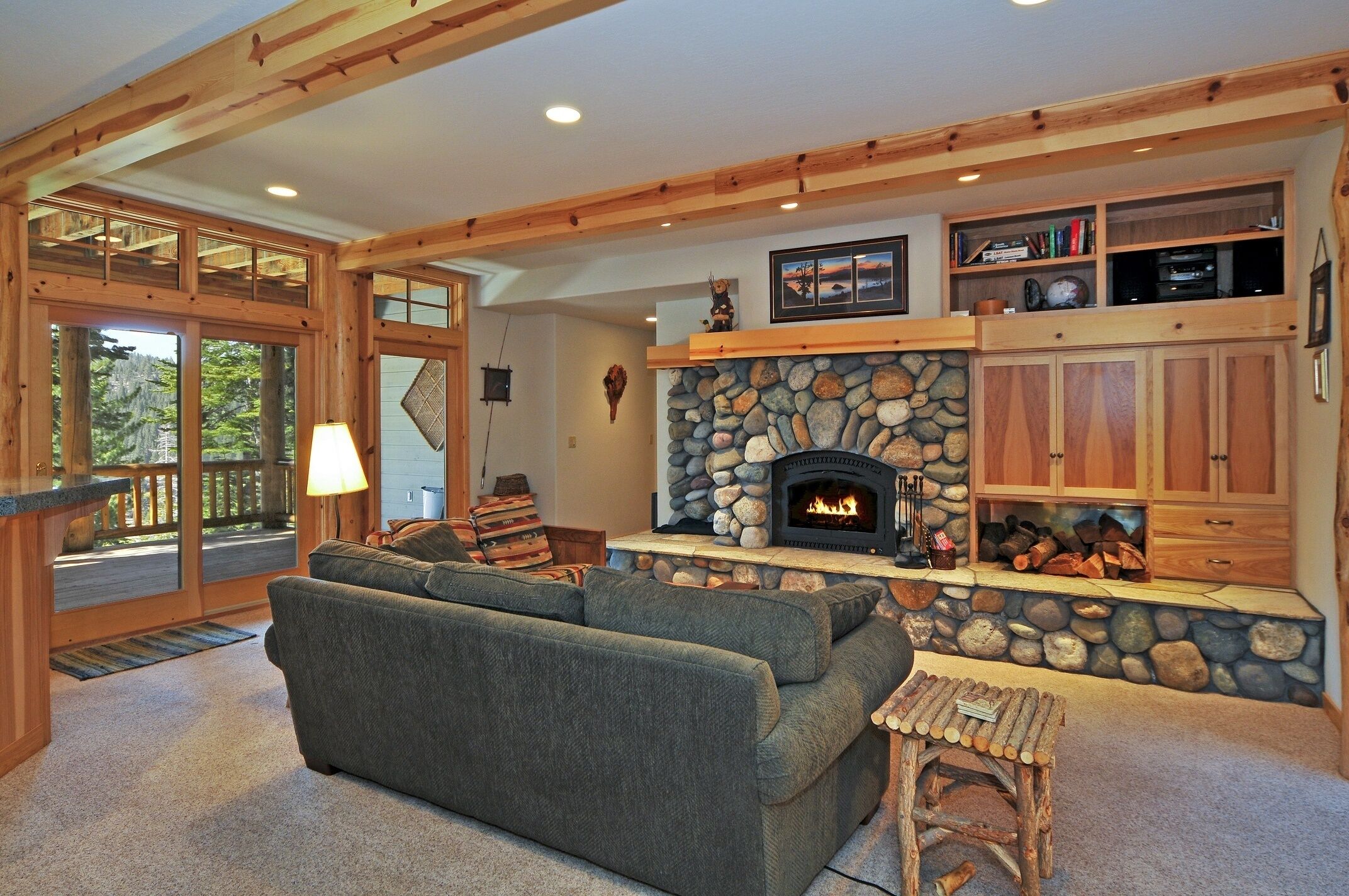 A cozy living room with a stone fireplace, wooden beams, and a large gray sofa.