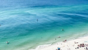 Uma praia com águas turquesa cristalinas, areal arenoso e pessoas praticando diversas atividades.